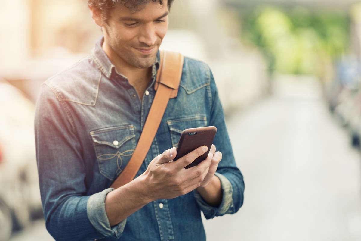 Homme regarde son téléphone et sourit, content avec nouveau forfait 50 Go de Cdiscount Mobile