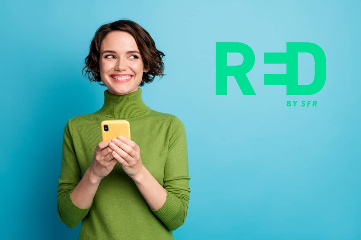 Femme en pull vert avec smartphone dans les mains, sourit car elle a le choix entre 2 forfaits 5G à moins de 10€ chez RED by SFR