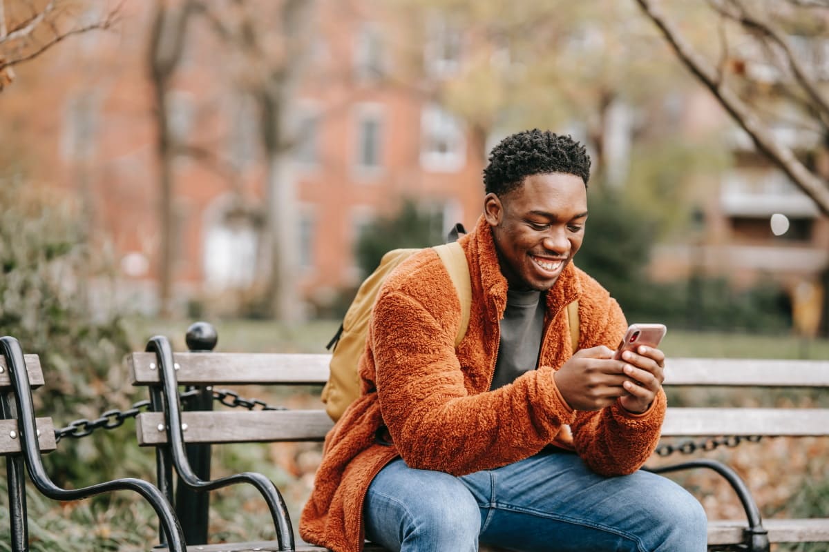 Homme assis sur un banc dehors avec un smartphone et un grand sourire car 2 nouveaux forfaits chez Cdiscount Mobile