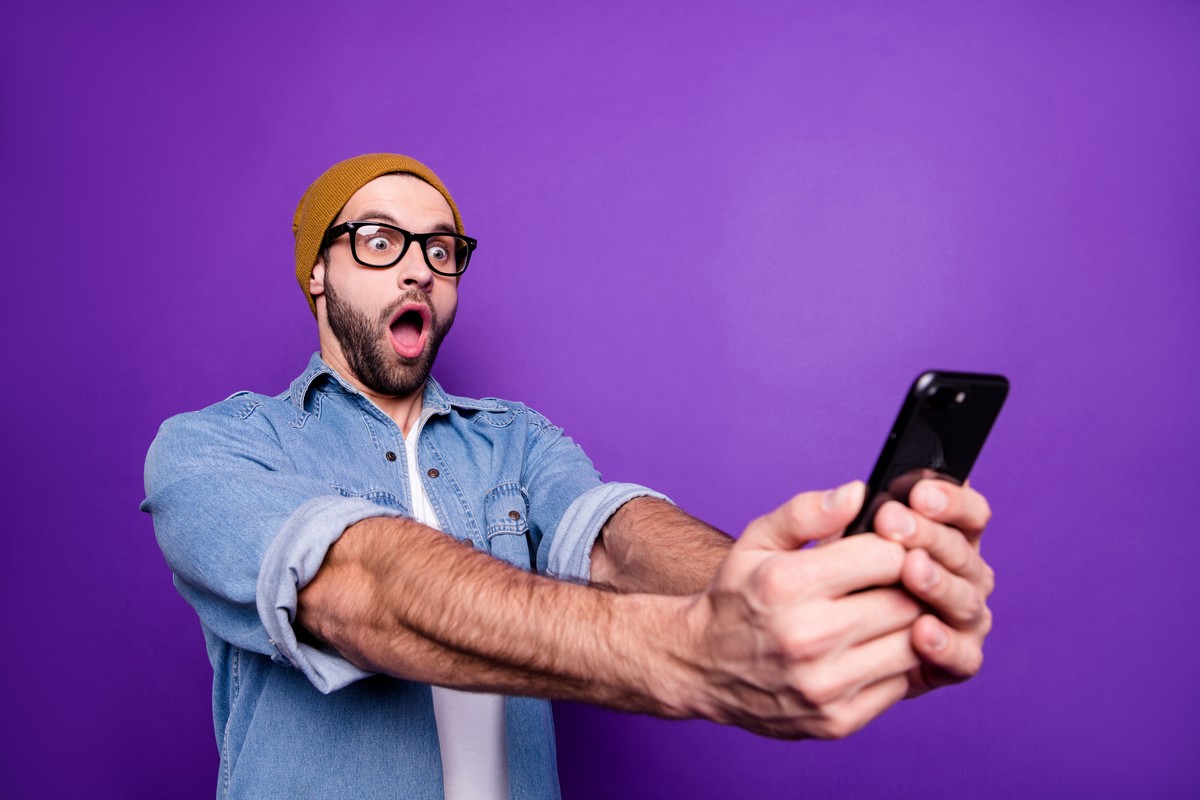 Homme avec smartphone sur fond violet bouche bée de surprise devant nouveau forfait de 160 Go de Cdiscount Mobile à 10€