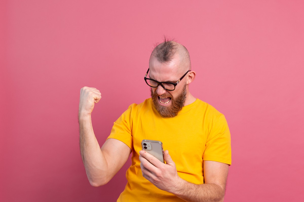 Homme avec smartphone serre le poing en signe de victoire, car il possède la plus grosse enveloppe Internet en 5G pour 10€/mois