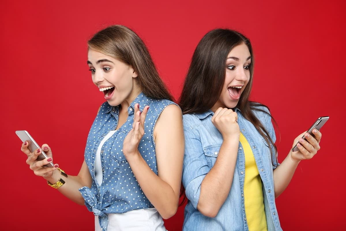 2 filles dos à dos avec smartphone, ravies de leur forfait mobile gratuit, chez Orange et chez Free