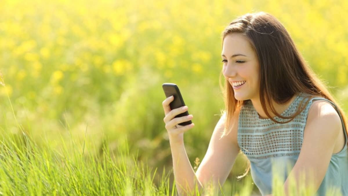 Fille dans un champ de fleurs jaunes avec son smartphone, ravie de son forfait 50 Go de Lebara
