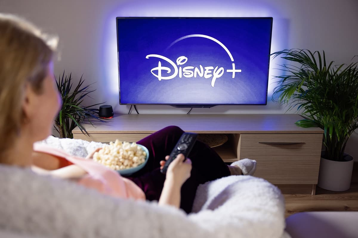 Femme dans son canapé devant télé avec logo Disney+, qui met fin au partage de compte gratuit