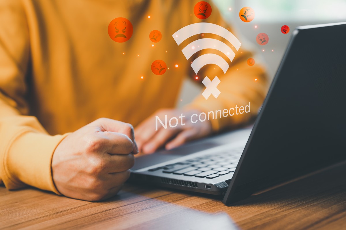 Homme fâché poing sur la table près PC portable, avec logo Wi-Fi rouge "not connected"